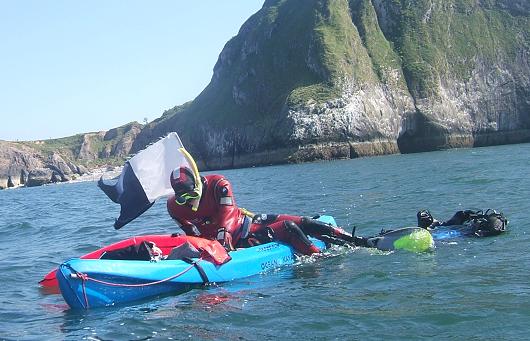 Scuba diver climbs back onto his kayak after surfacing from a dive; will load up gear and head back to shore