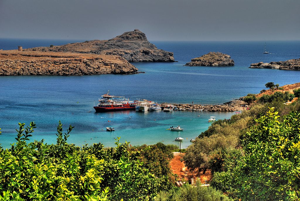 The clear blue waters of Lindos Bay filled with boats surrounded by lush greenery and a rocky coastline